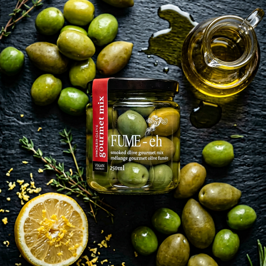 Jar of Fume olives surrounded by green olives, lemon, and herbs on a dark surface